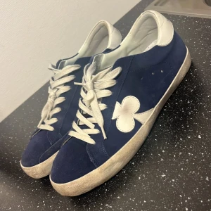 Blå sneakers från The Gallerist - Snygga blå sneakers från The Gallerist med vita detaljer och snörning. Skorna är använda runt 10-15 gånger så i mycket bra skick. Kolla på hemsidan så ser ni att de är smuts liknade design.