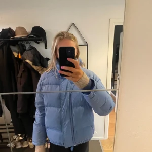 Blå pufferjacka från Re:Down - Säljer en blå pufferjacka från Re:Down, tillverkad av 100% återvunnet dun och fjädrar. Jackan är lätt och har en dragkedja framtill. Perfekt för kyliga dagar med sin vind- och vattenavvisande funktion. Har små fläckar men syns lite när man har den på. 
