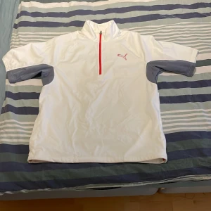 Vit och grå tröja från Puma - Säljer en vit tröja från Puma med grå detaljer på ärmarna och en röd dragkedja. Perfekt för sportiga aktiviteter eller en avslappnad stil. Vindväst i mycket bra skick. Pris går alltid att förhandlas.
