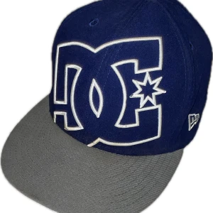 Blå och grå keps från DC - Snygg blå keps med grå skärm från DC. Kepsen har en stor broderad logotyp framtill och justerbar passform baktill. Priset kan diskuteras 