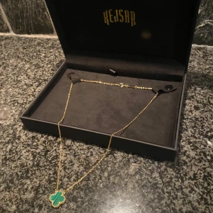 Guldhalsband med fyrklöverberlock - Elegant guldhalsband från Kejsar med en grön fyrklöverberlock. Perfekt för att lägga till en touch av lyx och färg till din stil. Halsbandet kommer i en stilren svart ask. Levererad idag, nypris 1499
