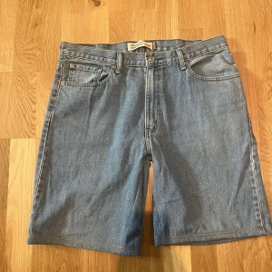 Blå jeansshorts från Levi's - Säljer ett par klassiska blå jeansshorts från Levi's. De har en normal passform med fem fickor och knappgylf. Perfekta för en avslappnad stil.