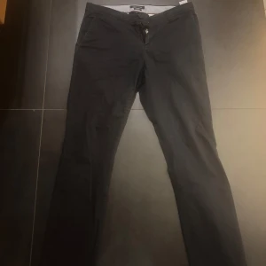 Svarta byxor från Tommy Hilfiger - Snygga svarta byxor från Tommy Hilfiger i slim fit. De har en klassisk design med knappar bak och bälteshällor. Perfekta för en stilren look.