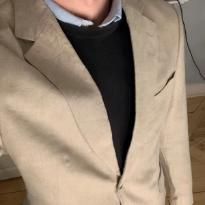 Beige linne kavaj från Tiger of Sweden - Snygg beige kavaj från Tiger of Sweden i 100% linne. Perfekt för en stilren look med två knappar framtill och klassiska fickor. Passar utmärkt till både formella och avslappnade tillfällen. Storlek 52 regular