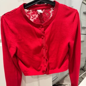 Super gullig röd kofta med spetsdetaljer - Snygg röd kofta med spetsdetaljer på ryggen och knappar framtill. storlek 158/164. (Köparen står för frakten)