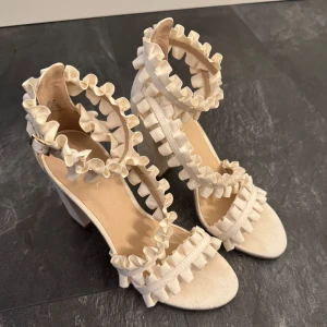 Beiga klackar med volanger - Helt nya och oanvända ivyrevel klackar. Har dock två fläckar från tuschpennor som ej syns när dem används, fläckarna är på insidan av klackarna (se bilder). Har aldrig fått användning av dem och säljs därav. 