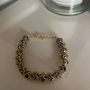 Guld och blått armband - Snyggt armband i guld och blått med ett unikt mönster. Perfekt för att ge en touch av elegans till vilken outfit som helst. Armbandet har en justerbar kedja för att passa olika storlekar. Perfekt för festliga tillfällen eller som en fin present.