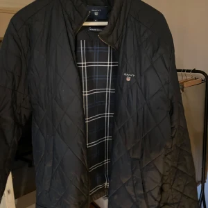 Svart quiltad jacka från GANT - Säljer en snygg svart quiltad jacka från GANT i storlek M. Jackan har en dragkedja framtill och ett stilrent rutigt mönster på insidan. Perfekt för höst och vår, med en klassisk look som funkar till det mesta. Passar både till vardags och lite finare tillfällen.