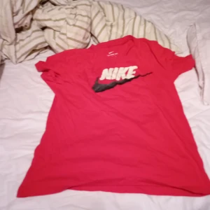 Röd Nike t-shirt - Säljer en röd Nike t-shirt i bomull med det klassiska Nike-loggan i vitt och svart på framsidan. Den är kortärmad och perfekt för både träning och vardag. Skön passform och i bra skick!