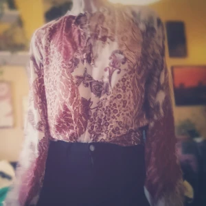 Vintage blus med retro mönster från Gina Tricot - Säljer en superfin tröja från Gina Tricot i storlek 36. Den har ett vackert retro mönster i rött och rosa med inslag av beige. Tröjan är perfekt för sommaren med sitt lätta och luftiga material. Den har snör detaljer vid halsen och är i nyskick.