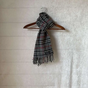 Burberry halsduk - Säljer en grå halsduk från Burberry. Den är i 100% kashmir. Perfekt för att hålla sig varm under höst och vinter. Den har ett stilrent mönster med inslag av rött och svart. Passar både till vardags och festliga tillfällen. Är perfekt nu i vinter och höst. Denna är i skick 9/10 utan defekter och såklart äkta. Vid frågor är det bara att höra av sig👍