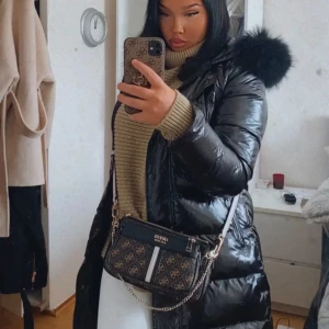 Svart gloss dunjacka med pälskrage - Snygg svart glansig dunjacka med en fluffig pälskrage. Jackan har långa ärmar och en dragkedja framtill. Perfekt för kalla dagar när du vill hålla stilen. Säljer pågrund av att jag ej använder den längre. Är i relativt bra skick med små defekter. Köpt från feminina i storlek M, skulle dock säga att den passar storlek S också. 