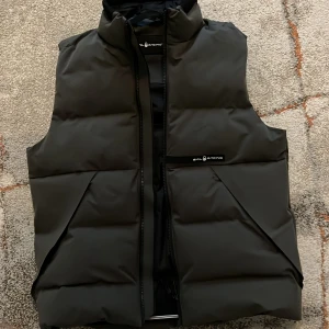 Svart dunväst från Sail Racing - Snygg svart dunväst från Sail Racing med dragkedja framtill. Perfekt för kyligare dagar med sin quiltade design som håller värmen. Västen har en stilren look och passar bra till olika outfits. Ny pris 2500 mitt pris 1200. Kan gå ner i pris, tveka inte på att fråga