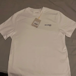 Vit t-shirt från Axel Arigato - Säljer en helt ny stilren vit t-shirt från Axel Arigato med tryck på bröstet. Säljer den för 800 kr.