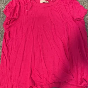 Rosa t-shirt från Lindex - Säljer en härlig rosa t-shirt från Lindex. Den har korta ärmar och är perfekt för en avslappnad stil. Gjord i ett mjukt material som känns skönt mot huden.