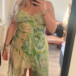 Grön mönstrad klänning - Säljer en unik grön mönstrad klänning med ett abstrakt mönster. Klänningen har smala axelband och en asymmetrisk design som ger en bohemisk känsla av 2000-tal. Passar bäst M
