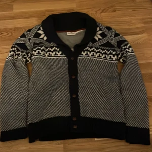 Svart och vit kofta från Shine Fashion - Säljer en snygg svart och vit kofta från Shine Fashion med ett klassiskt mönster. Koftan har långa ärmar och knappar framtill. Perfekt för kyliga dagar.