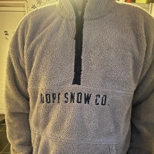 Beige fleece hoodie från Dope Snow Co. - Säljer en beige fleece hoodie från Dope Snow Co. med halv dragkedja och broderad logga på bröstet. Perfekt för kyliga dagar med sin mjuka och varma känsla. Den har långa ärmar och en hög krage för extra värme.