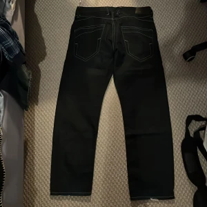 Svarta jeans från Selected Homme - Snygga svarta jeans från Selected Homme med klassisk femficksdesign. De har en knappgylf och är perfekta för en stilren look. Passar bra till både vardag och mer uppklädda tillfällen. Är lite osäker på storlek så hör av er!