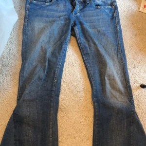 Blå bootcut jeans från G-Star - Snygga blå bootcut jeans från G-Star med knappar och dragkedjor som detaljer. Perfekta för en avslappnad stil med en touch av edge. Klassisk femficksdesign och lågmidjade för en utsvängd passform.