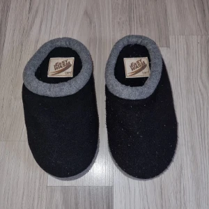 Svarta tofflor från Easy Wash - Mysiga svarta tofflor från Easy Wash med grå kant. Perfekta för att hålla fötterna varma hemma. De har en mjuk och bekväm design med en slitstark sula.