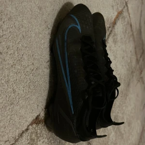 Svarta fotbollsskor med blå detaljer - Snygga svarta fotbollsskor med blå detaljer och snörning. Perfekta för fotbollsplanen med en stilren design och bra passform. Ny pris 3000 mitt pris 600