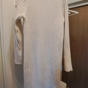 Creme ribbad klänning från H&M - Säljer en stilren creme ribbad klänning från H&M. Den har långa ärmar och en bekväm passform som är perfekt för kyligare dagar. Polokrage.Klänningen är gjord i ett mjukt blandmaterial som känns skönt mot huden. Perfekt för en mysig och chic look!