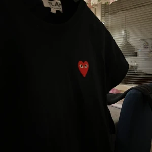 Svart t-shirt från play  - Säljer en svart t-shirt från Comme des Garçons med det ikoniska röda hjärtat med ögon på bröstet. T-shirten har en klassisk passform och är kortärmad. Perfekt för en stilren look.