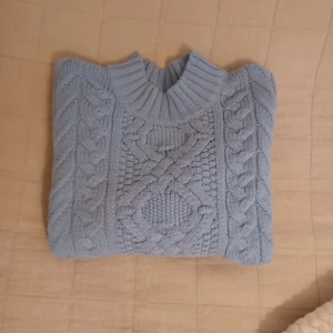 Ljusblå stickad tröja - Mysig ljusblå stickad tröja från Lager 157 med ett snyggt flätmönster på framsidan. Tröjan har långa ärmar och en ribbad krage som ger extra värme. Perfekt för kyliga dagar! Passar även s/m