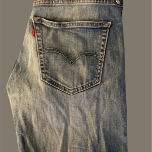 Blå jeans med slitningar - Säljer ett par klassiska blå jeans från Levi's med coola slitningar och en avslappnad look. Perfekta för en casual stil. De har en femficksdesign och knappgylf.