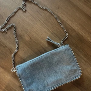 Jeansväska med kedja - Snygg jeansväska med kedjedetaljer och dragkedja. Perfekt för att ge din outfit en cool touch. Väskan har flera fack för enkel organisering och en stilren design.