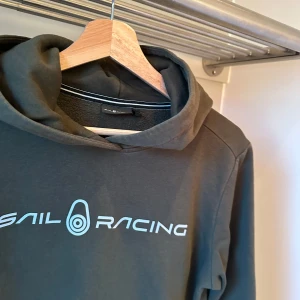 Grön hoodie från Sail Racing - Säljer en snygg grön hoodie från Sail Racing med logotyp på bröstet och en mindre logotyp på huvan. Perfekt för en avslappnad stil. Hoodien har långa ärmar och en klassisk passform. Ny pris: 1300kr