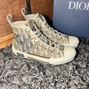 Höga sneakers från Dior - Snygga höga sneakers från Dior med genomskinligt material och ikoniskt mönster. Skorna har snörning och en vit sula. Perfekta för att ge din outfit en lyxig touch.