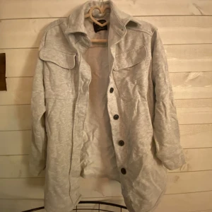 Grå jacka från Newyorker  - Säljer en stilren grå jacka från Newyorker. Jackan har långa ärmar och knappar framtill. Den är designad med två bröstfickor med lock och har en klassisk krage. Har bara prövats 1 gång. 