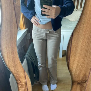 Beige byxor från Embargo bootcut - Snygga beige byxor från Embargo med bootcut-stil. De har en lågmidjad passform och är perfekta för en avslappnad look. Byxorna har en dragkedja och knapp framtill.