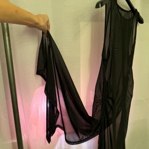 Svart transparent klänning - Säljer en svart transparent klänning i ett lätt och luftigt material. Klänningen är ärmlös och har en rund halsringning. Perfekt för lager-på-lager styling eller som ett statement-plagg.