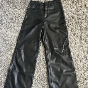 Svarta skinn byxor från H&M - Snygga svarta byxor i syntetmaterial från H&M. De har en hög midja och en vid passform, vilket ger en modern look. Perfekta för att skapa en stilren outfit.🙌🏻🖤