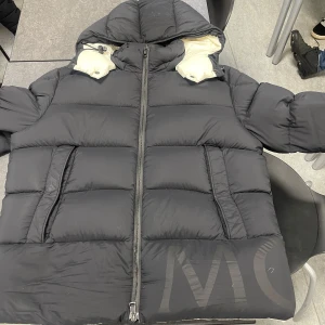 Moncler jacket - Säljer en äkta Moncler dunjacka i storlek L. Färgen är svart med diskret Moncler-logga pả nedre delen. Jackan är tjock och varm, perfekt för vintern, och har en stilren design med en huva och högkvalitativt material. Den är i bra skick och mycket skon att bara. Skicka ett meddelande vid intresse!