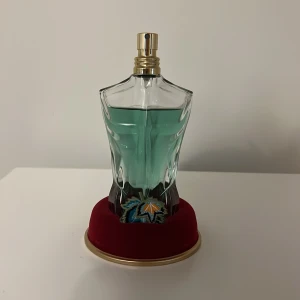 Parfymflaska paradise garden - Unik parfymflaska i form av en manlig torso med en turkos vätska inuti. Flaskan står på en röd bas och har en elegant guld spraytopp. Perfekt för den som vill ha en iögonfallande och stilren design på sin parfym. Säljer då jag inte använder längre, luktar gott och funkar som den ska.
