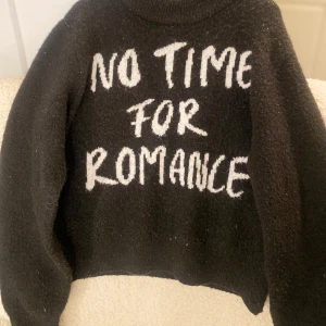 Svart stickad tröja med text - Säljer en svart stickad tröja med texten 'NO TIME FOR ROMANCE' i vitt på framsidan. Tröjan har långa ärmar och en hög krage, perfekt för en avslappnad stil. Passar bra till jeans eller kjol för en cool look.