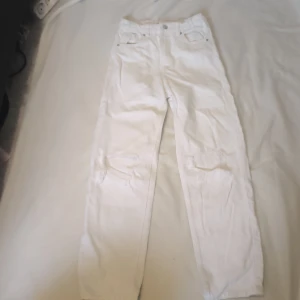 Vita jeansbyxor från Gina Tricot - Snygga vita jeansbyxor från Gina Tricot med slitna detaljer på knäna. De har en klassisk femficksdesign och en rak passform. Perfekta för en trendig look.