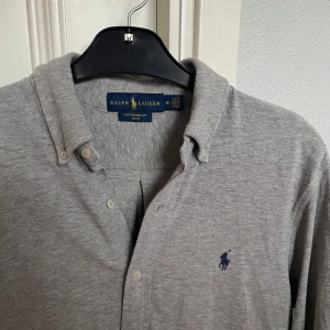 Grå skjorta - Ralph Lauren - Grå skjorta från Ralph Lauren i featherweight mesh. Skick: 9/10. Storlek: M. Kontakta oss för fler bilder eller info!🙌