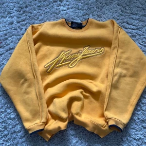 Gul sweatshirt från Karl Kani - Säljer en cool gul sweatshirt från Karl Kani med deras logga broderad på framsidan. Tröjan har långa ärmar och en rund halsringning med mörkblå detaljer vid muddar och krage. Perfekt för en avslappnad outfit. 