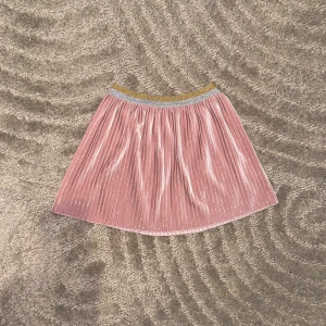 Rosa glittrig kjol (flickkjol) - Säljer en söt rosa glittrig flickkjol med elastisk midja i guld och silver. Kjolen har ett plisserat mönster som ger en fin volym och glans. Perfekt för att lysa upp vilken outfit som helst! 🌟