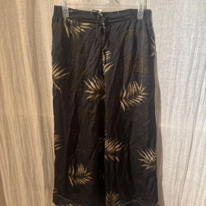 Svarta byxor med bladmotiv från Intimissimi - Snygga svarta byxor från Intimissimi med ett stilrent bladmotiv i beige. Byxorna har en loose passform och är försedda med snörning i midjan för extra komfort. Perfekta för en avslappnad stil.