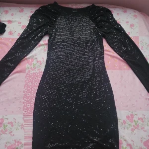 Svart glittrig klänning - Snygg svart klänning med glittrigt mönster och långa ärmar. Perfekt för en kväll ute med vänner. Klänningen har en tight passform som framhäver figuren. Har använt den bara en gång.