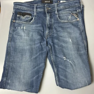 Blå jeans från Replay - Snygga blå jeans från Replay med slitna detaljer och en klassisk femficksdesign. De har en knappgylf och en bekväm passform som passar perfekt till vardags. Märkeslogga på bakfickan ger en extra touch. 33-33
