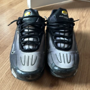 Nike Air Max sneakers - Snygga Nike Air Max sneakers i svart och grått med klassisk snörning. Skorna har en futuristisk design med Tuned Air-dämpning och tydliga detaljer på hälen. Perfekta för en sportig look.