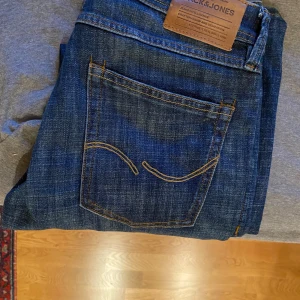 Blå jeans från Jack & Jones - Snygga blå jeans från Jack & Jones med klassisk femficksdesign och kontrastsömmar. Perfekta för en avslappnad stil. Märket 'Glenn' syns på insidan av midjan.    Strl: L/29 W/30     Har används väldigt fåtal gånger, är nästan som ett par nya jeans.   Skicket: 10/10.     Är de några funderingar så är det bara och skriva PM