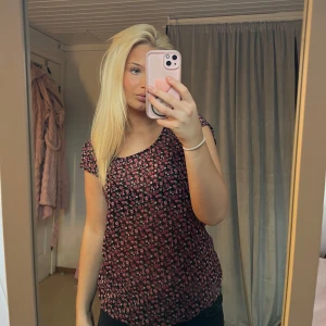 Blommig topp med korta ärmar - Säljer en söt blommig topp med korta ärmar. Toppen har ett mönster av små rosa blommor på en svart bakgrund. Perfekt för en avslappnad stil.